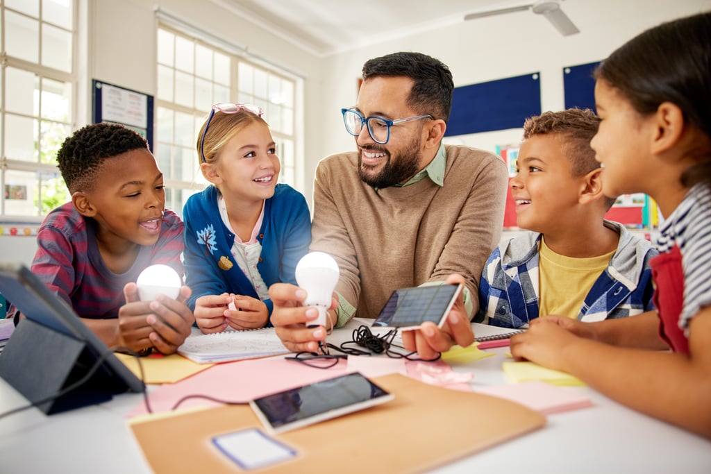 teacher with students around a table with lightbulbs and a tablet